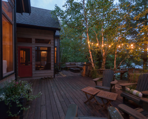 A beautiful outdoor deck with tasteful lighting outside of a lake home.
