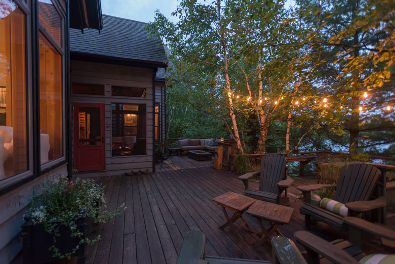 A beautiful outdoor deck with tasteful lighting outside of a lake home.
