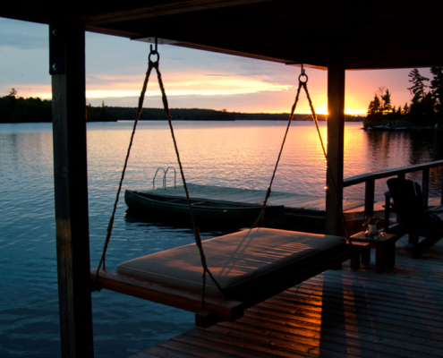 A summer sunset over a boat dock on a lake, surrounded by a forest.