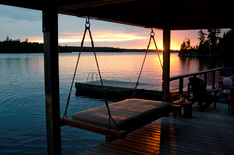 A summer sunset over a boat dock on a lake, surrounded by a forest.