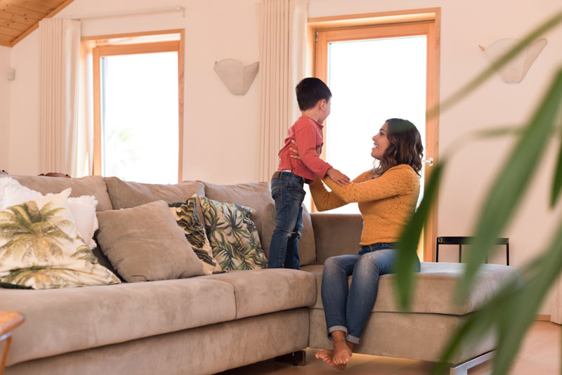 A woman sitting on the couch in the living room and playing with her son.