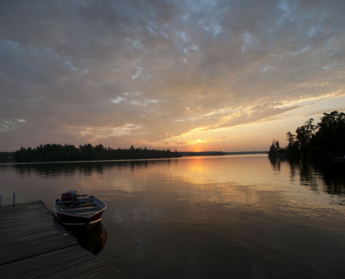 Sunset over a wooded lake with a boat dock.