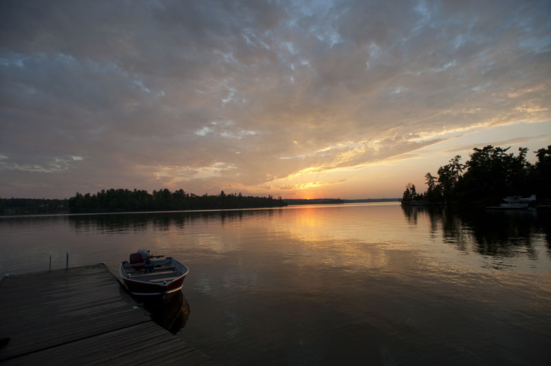 Sunset over a wooded lake with a boat dock.