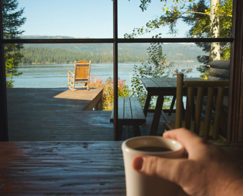 A lake viewed through a picture window in a lake home by a man drinking coffee.