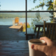 A lake viewed through a picture window in a lake home by a man drinking coffee.