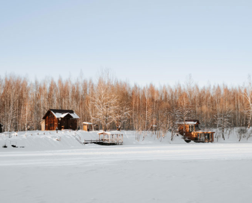A group of lake homes viewed from a snow-covered frozen lake in winter.