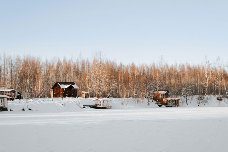 A group of lake homes viewed from a snow-covered frozen lake in winter.